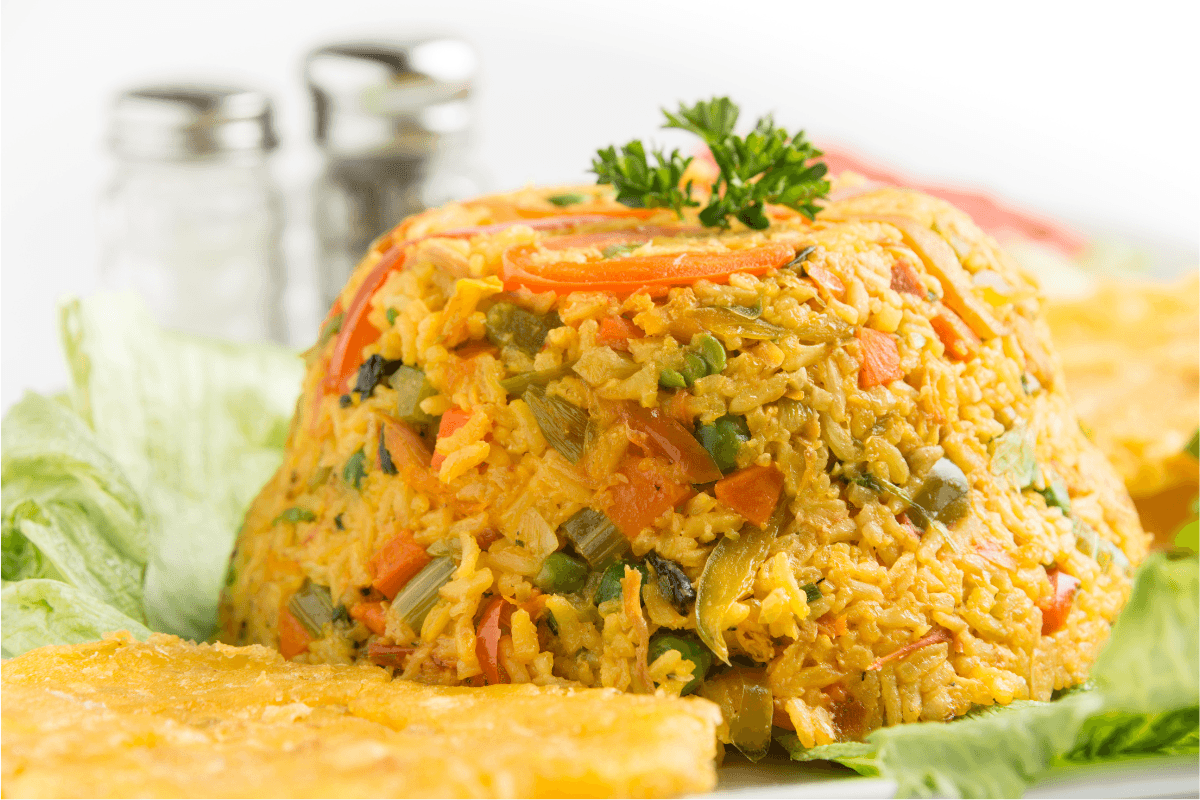Arroz Imperial: A Layered Cuban Comfort Dish 1 Arroz Imperial recipe featuring a vibrant layered dish of fluffy yellow rice, shredded chicken, creamy mayonnaise, peas, and red peppers, garnished with lemon wedges. Served alongside fresh ingredients.