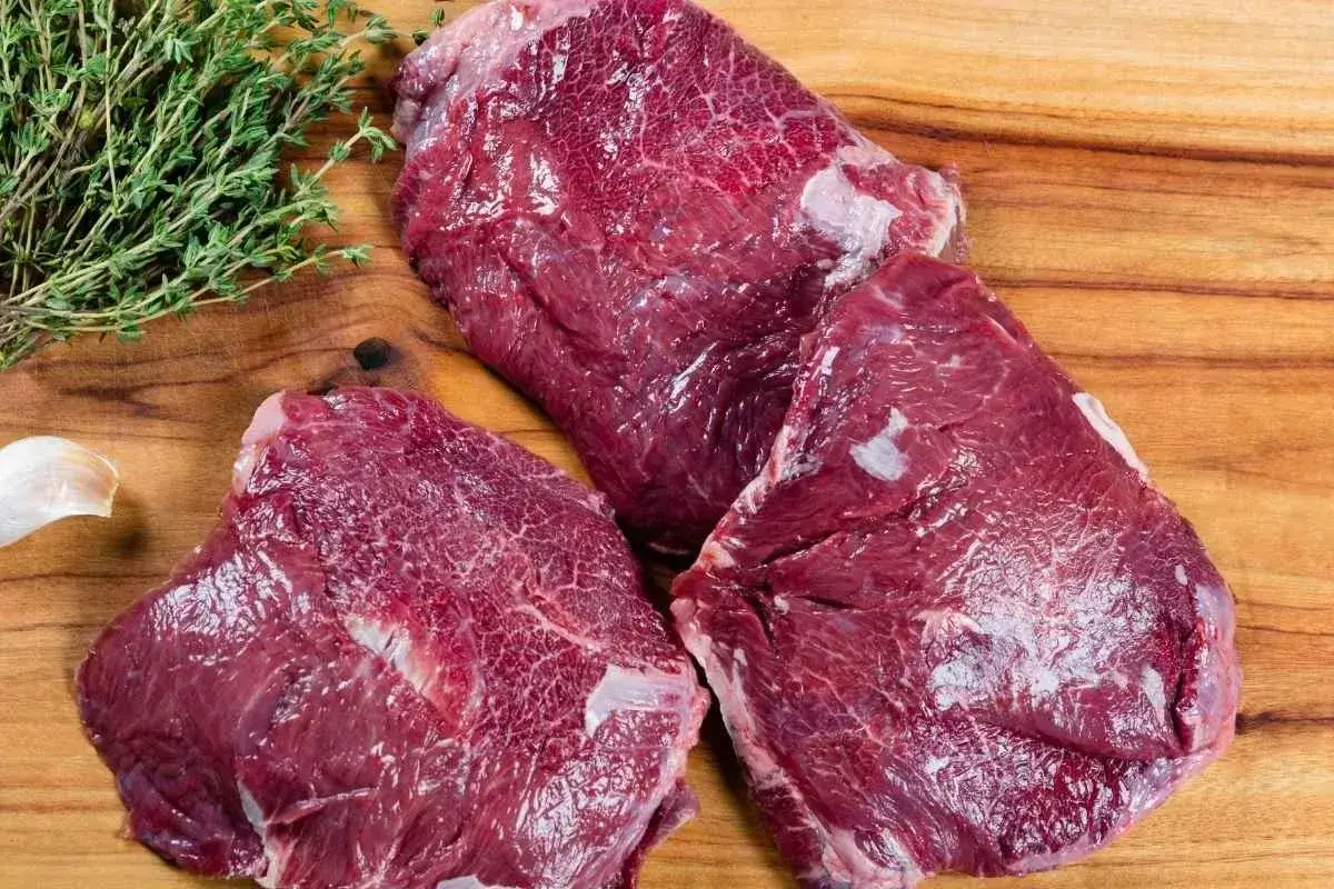 What Are Beef Cheeks Called in the USA? An In-depth Exploration 1 2 raw beef cheek pieces on a white surface with small bowls of salt, black pepper, cumin, and paprika arranged neatly beside them