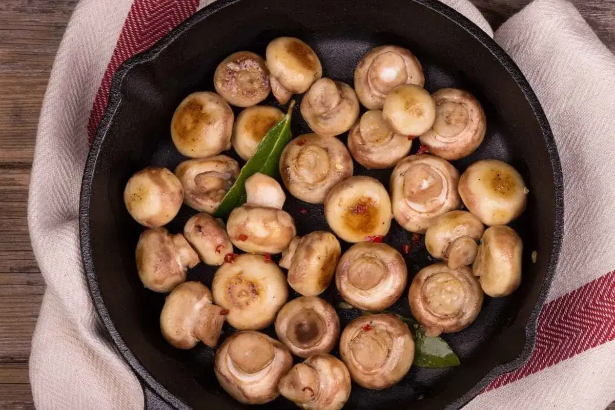 What is the Best Way to Eat Button Mushrooms? 1 Mushrooms being sautéed in a pan with garlic butter and parsley, with steam rising.