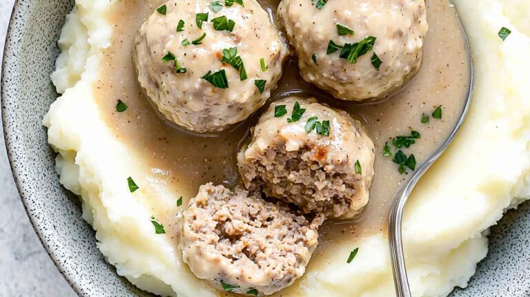 Crockpot Swedish Meatballs Recipe: The Easiest Way to Make Creamy, Tender Meatballs at Home 3 Creamy Crockpot Swedish meatballs served over mashed potatoes with parsley garnish, with one meatball cut open to show the inside.